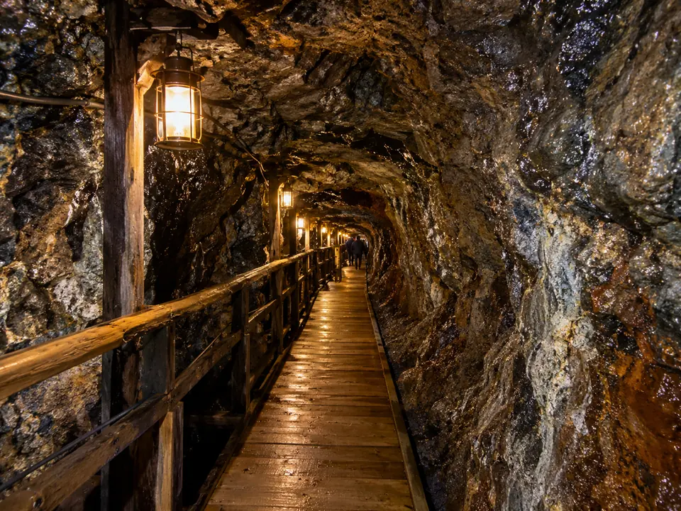 A narrow rock tunnel lit by lamps with a wooden walkway