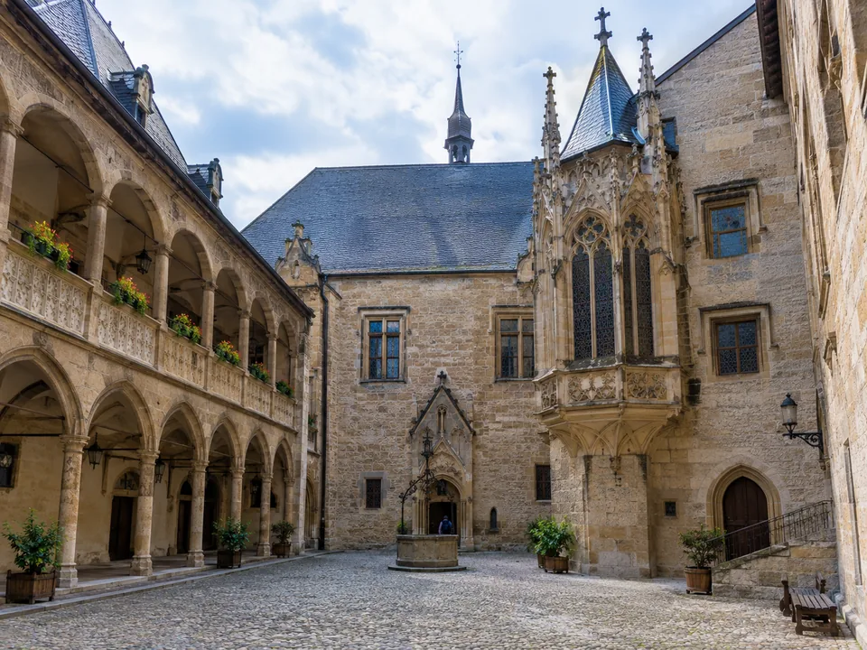 A stone courtyard with an arcade and a Gothic oriel chapel window