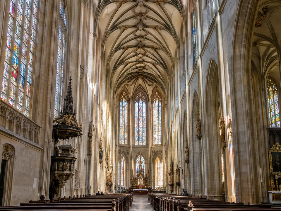 A ribbed Gothic net vault above tall stained-glass windows in a pale stone nave