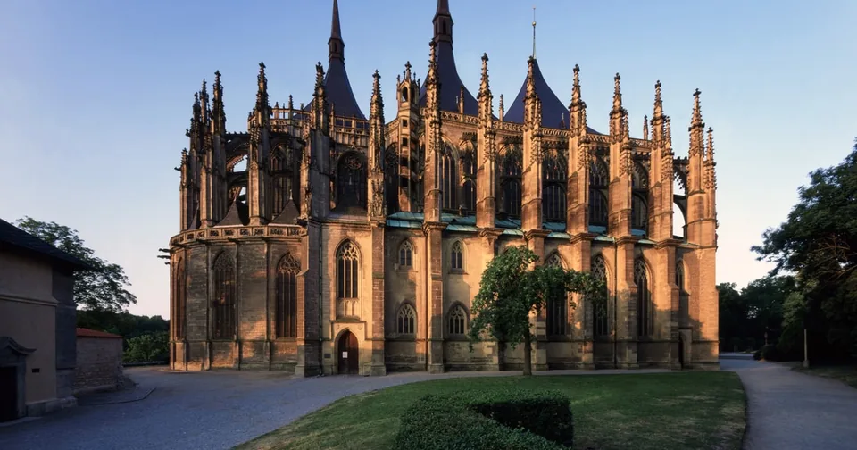 A Gothic cathedral with three tent-shaped spires at dusk